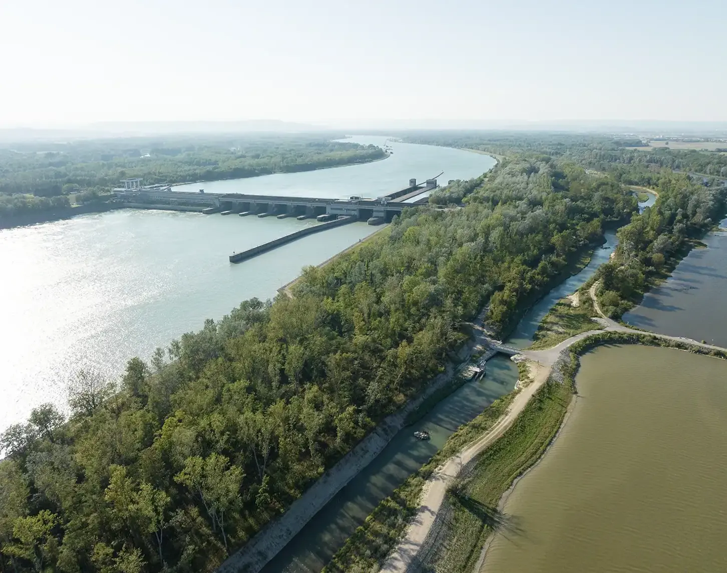 Blick auf das Kraftwerk Altenwörth. Man sieht die strahlend blaue Donau, Begrünung und die Fischwanderhilfe.